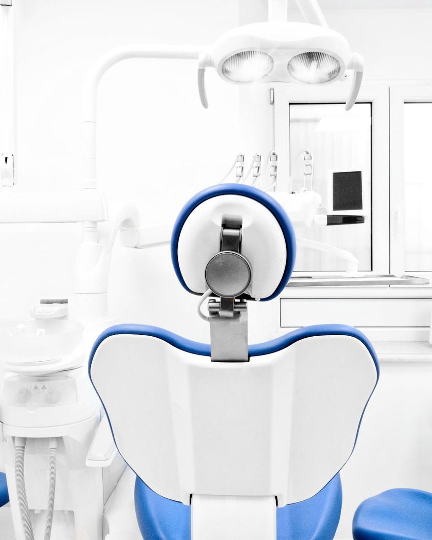 Una poltrona odontoiatrica bianca e blu vista da dietro, in una sala luminosa